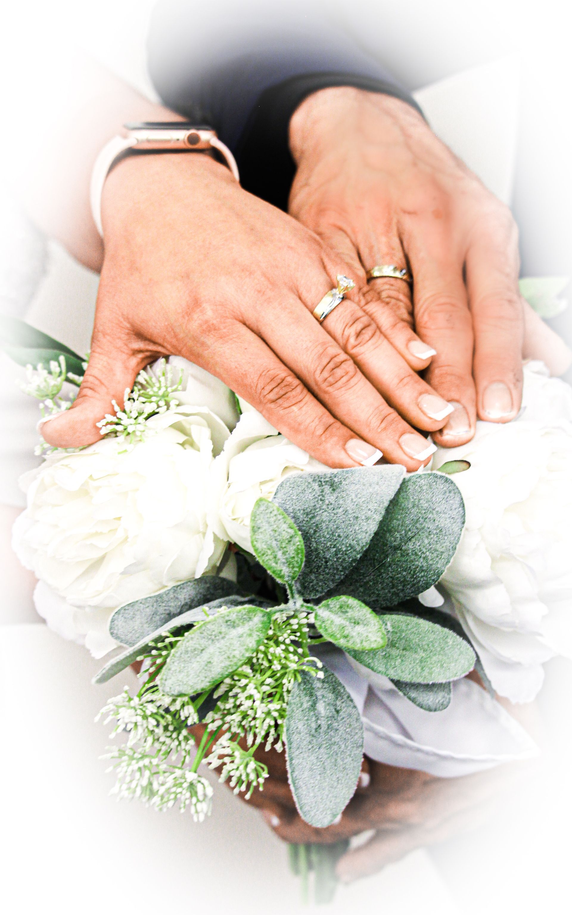 Hands with wedding rings over a bridal bouquet of white roses and greenery