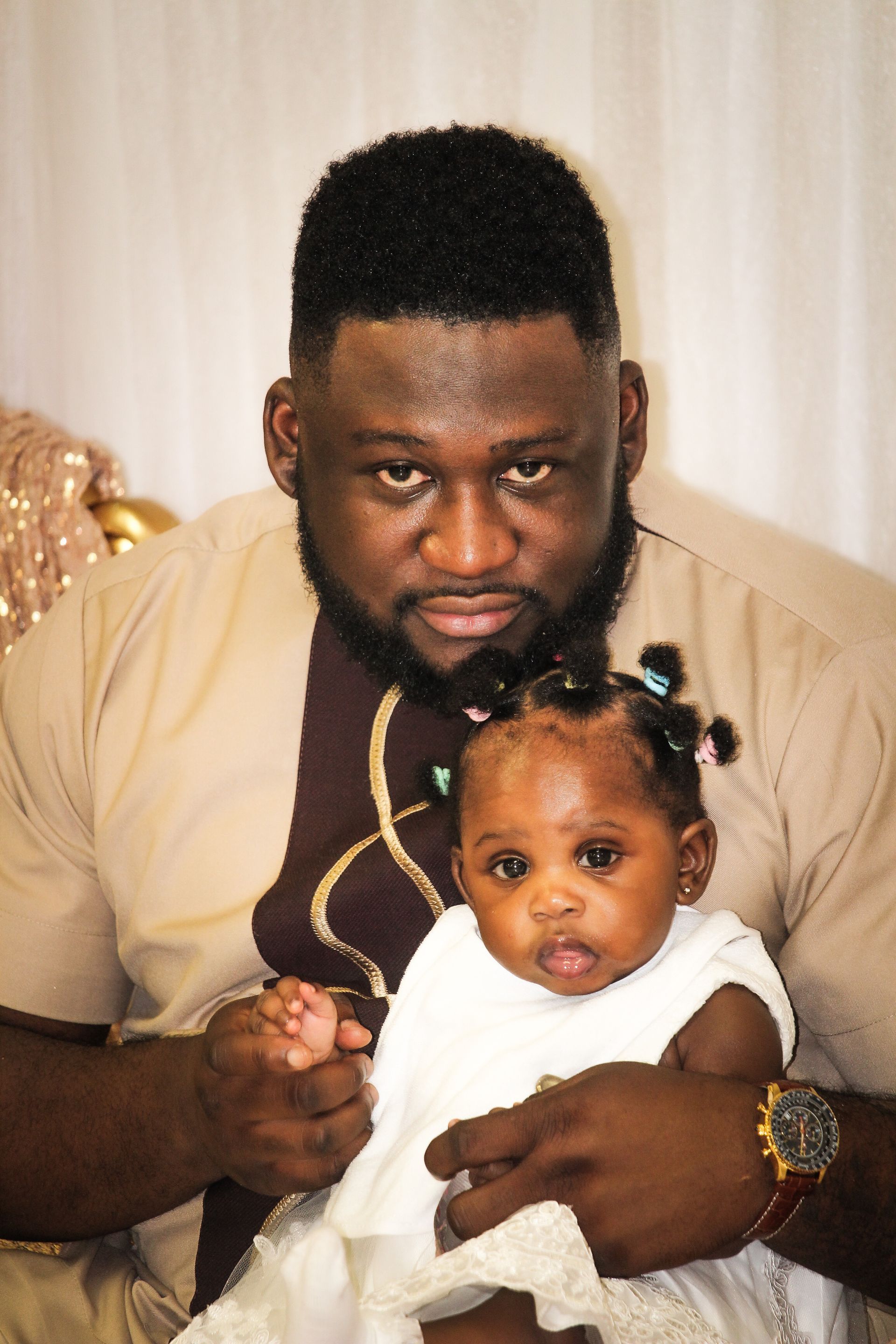 Man holding a baby on his lap indoors, both facing the camera.