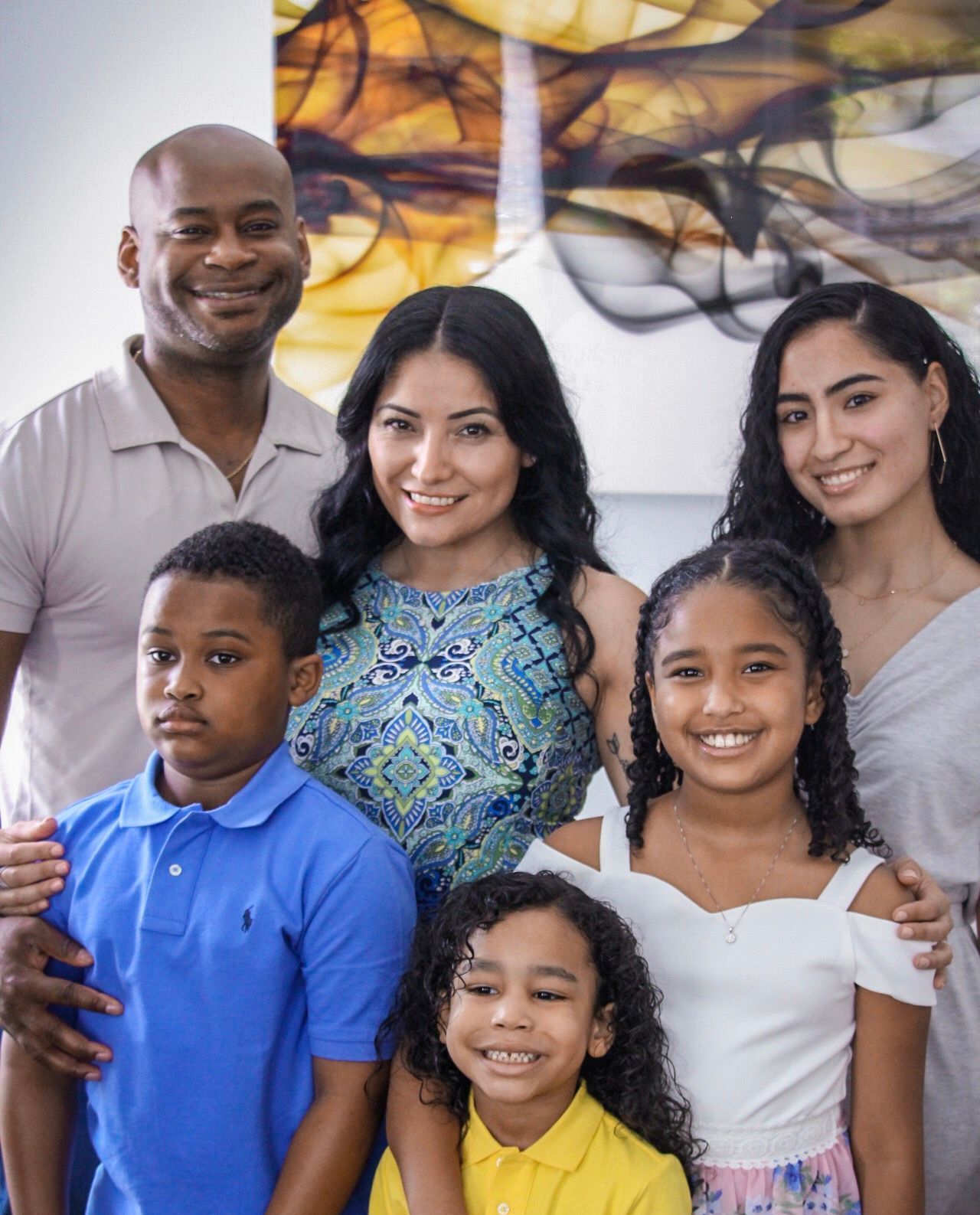 Smiling family of six posing indoors in front of colorful abstract wall art.