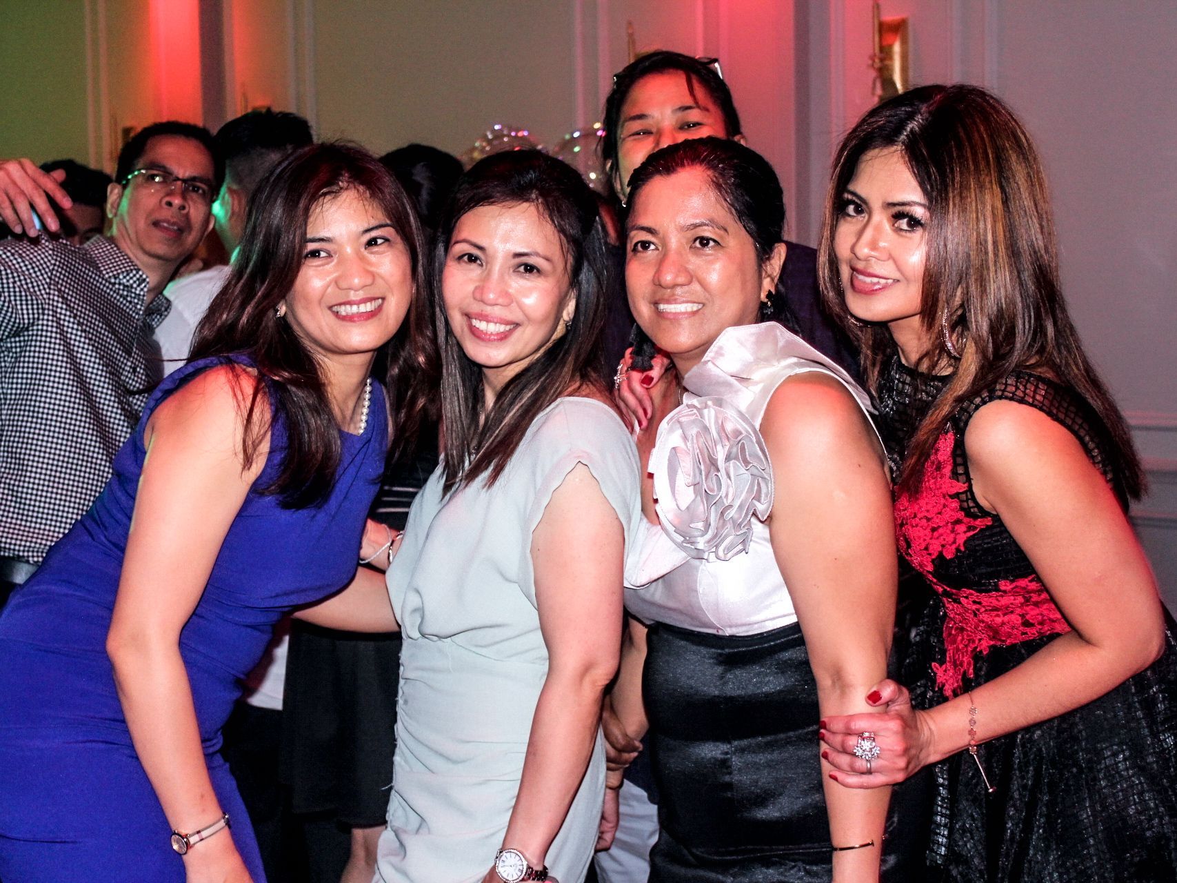 Five smiling people posing together at a party with pink lighting