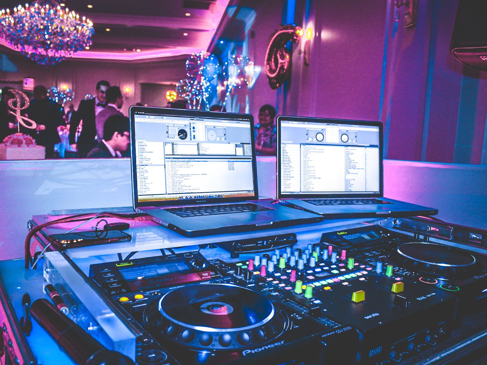 DJ booth with glowing mixer and twin laptops in a neon-lit club lounge