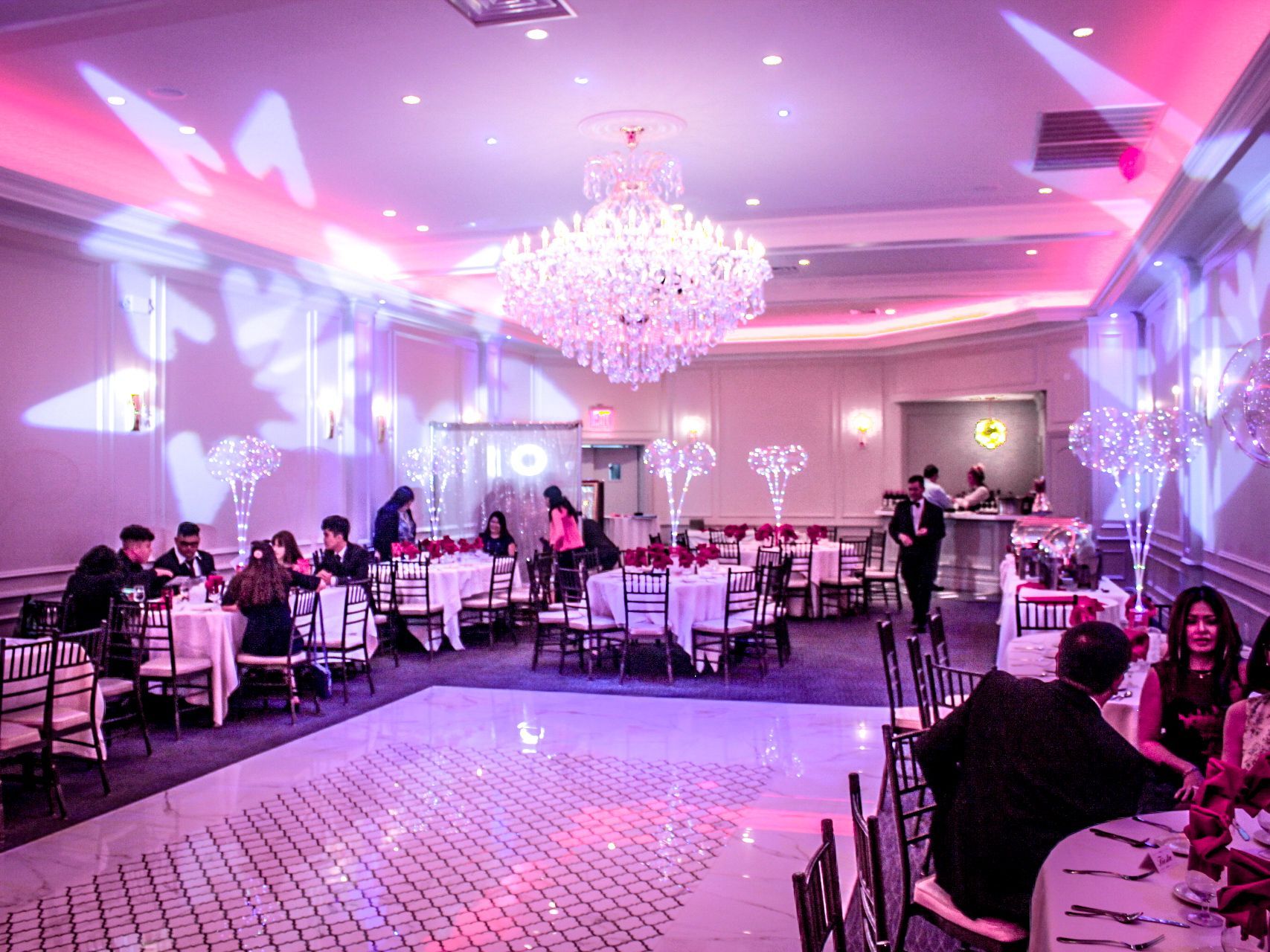 Elegant banquet hall with pink lighting, chandeliers, and guests seated at round tables during an event