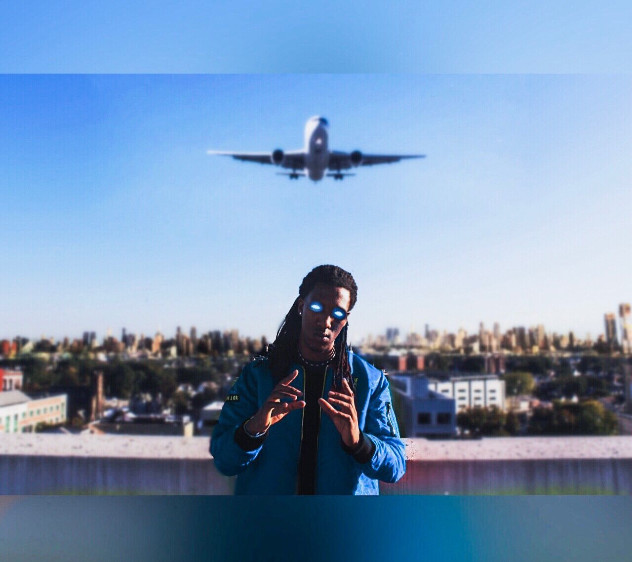 Man in blue jacket posing on a rooftop with a plane flying overhead against a city skyline