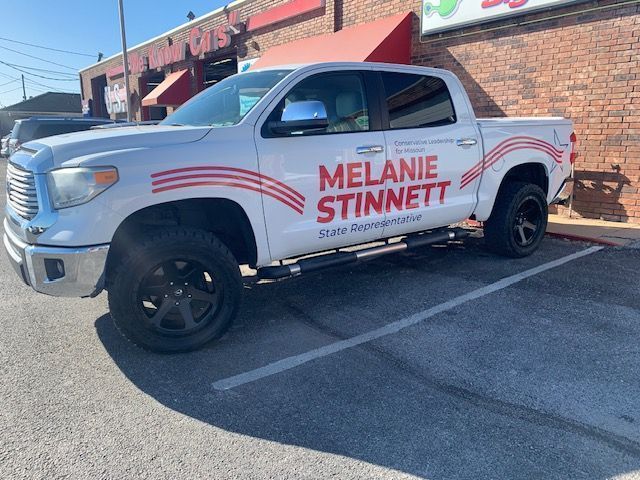 A White Truck With the Name Melanie Stinnett on the Side is Parked in a Parking Lot