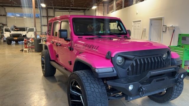 A pink jeep is parked in a garage.