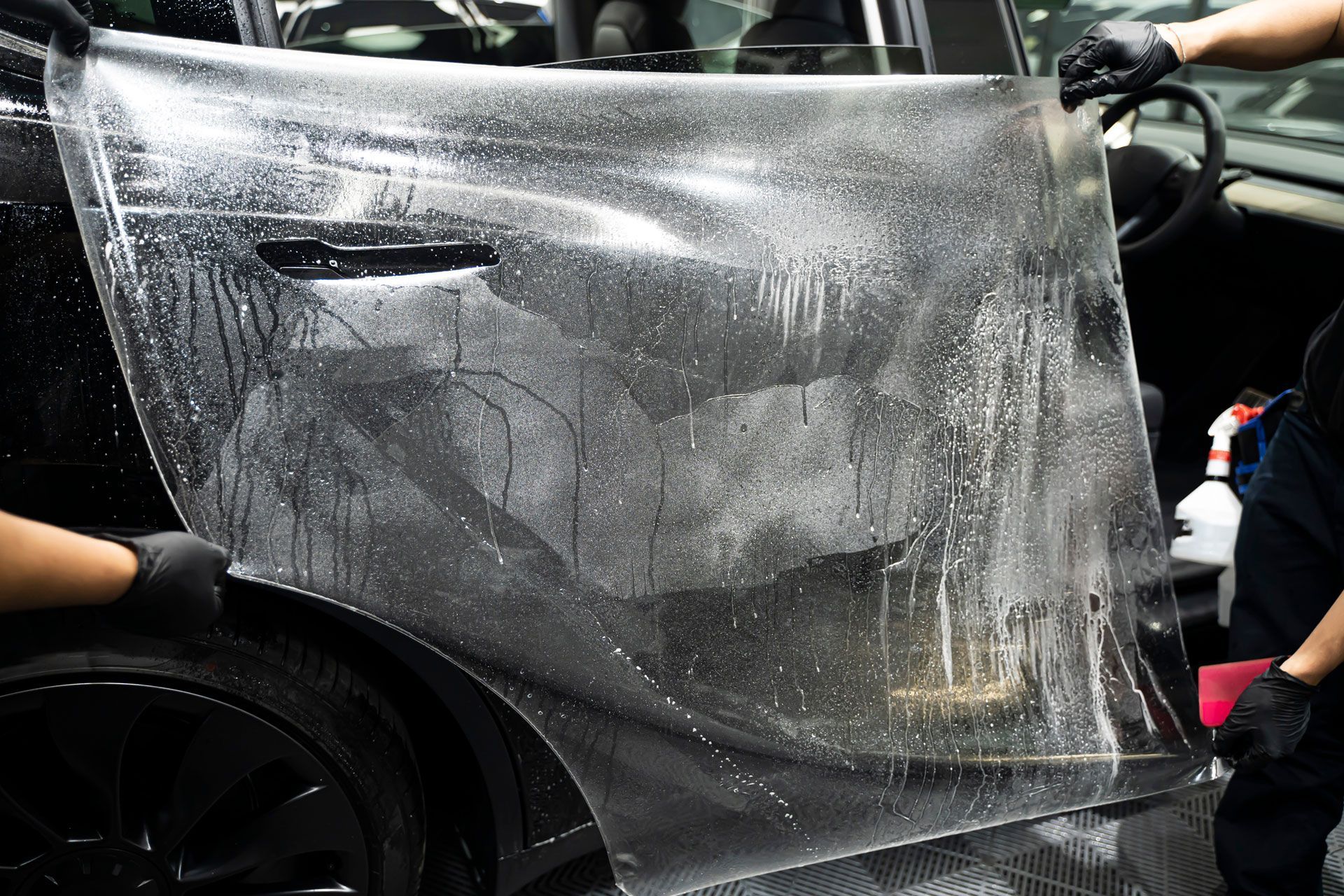 A person is applying a protective film to a black car.