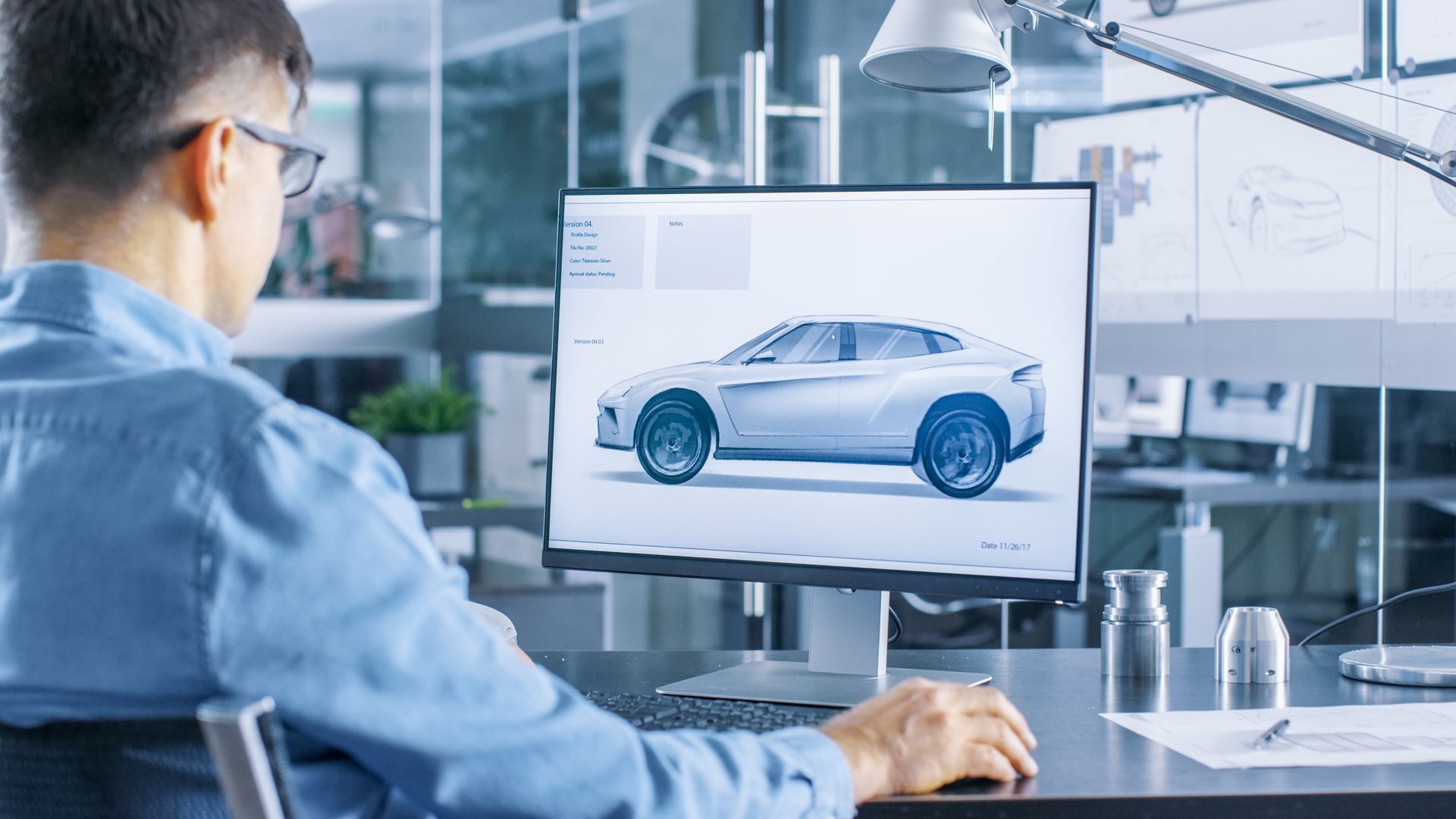 A Man is Sitting at a Desk Looking at a Computer Screen With a Car on It