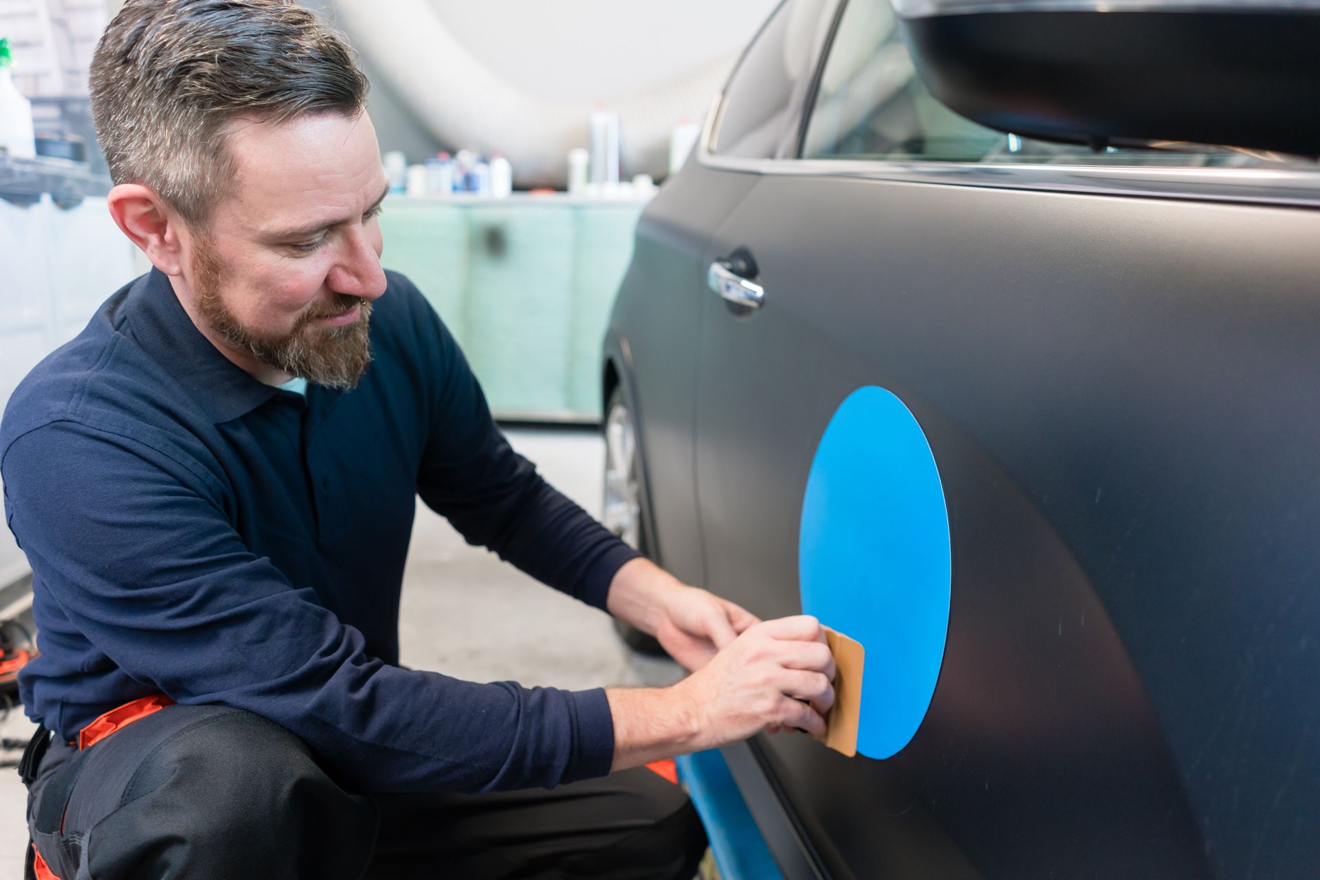 A Man is Wrapping a Car With a Blue Circle on It