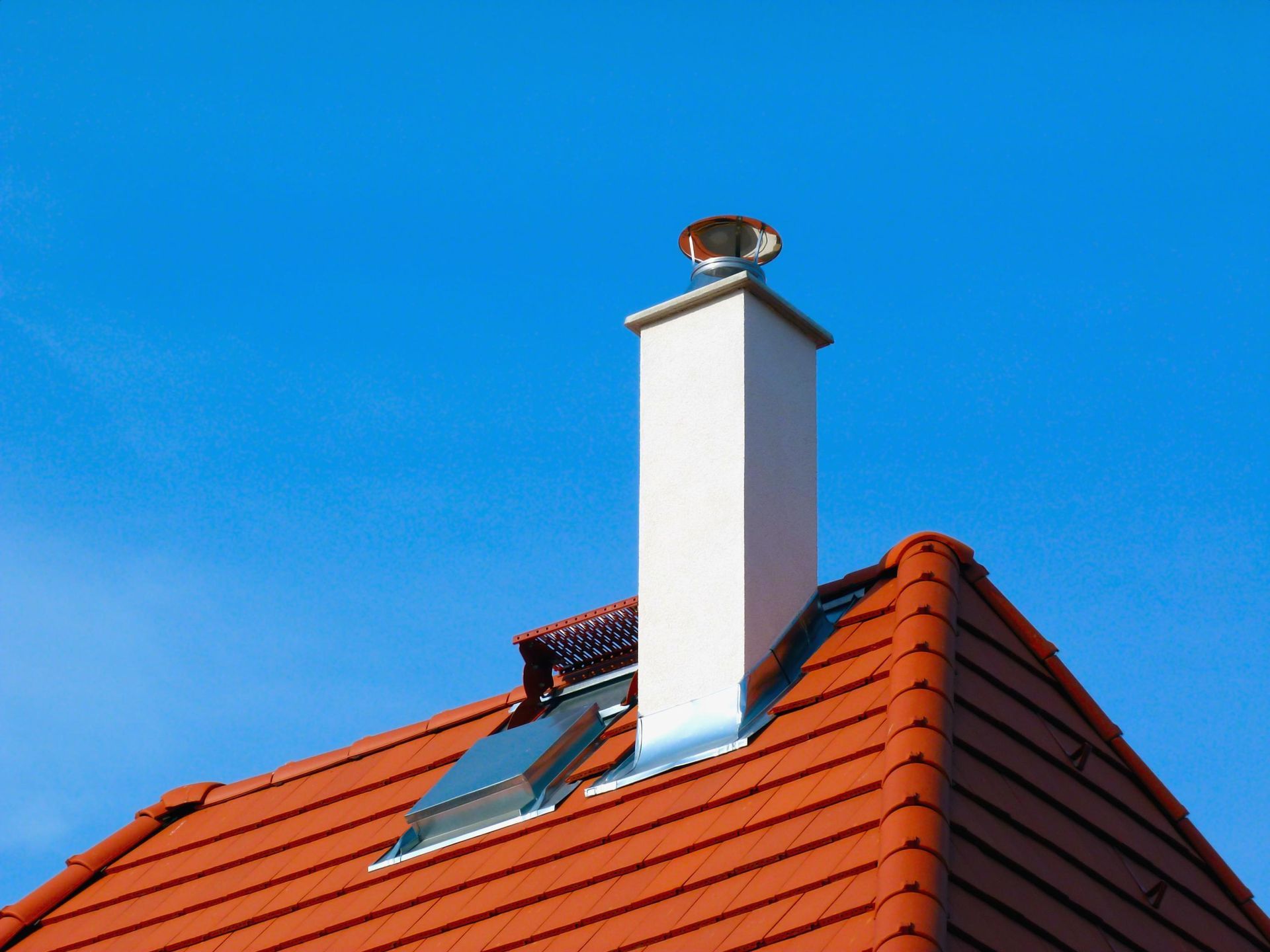 Red tiled roof with a white chimney against a clear blue sky