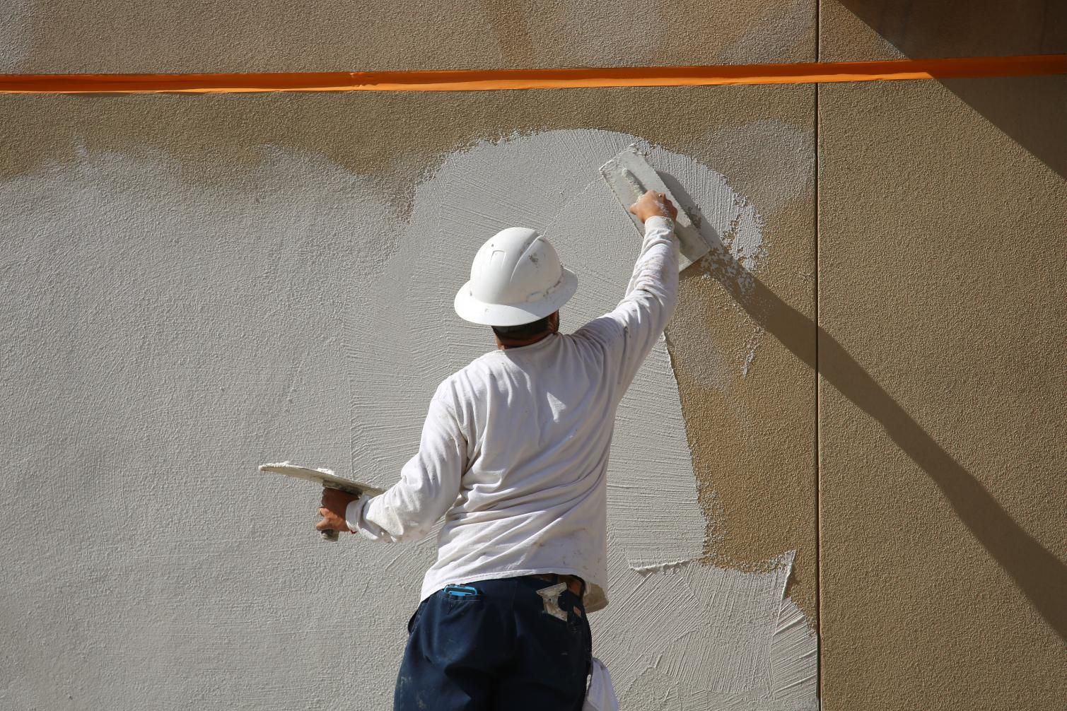 Worker in white hat painting a white patch on a textured wall outdoors