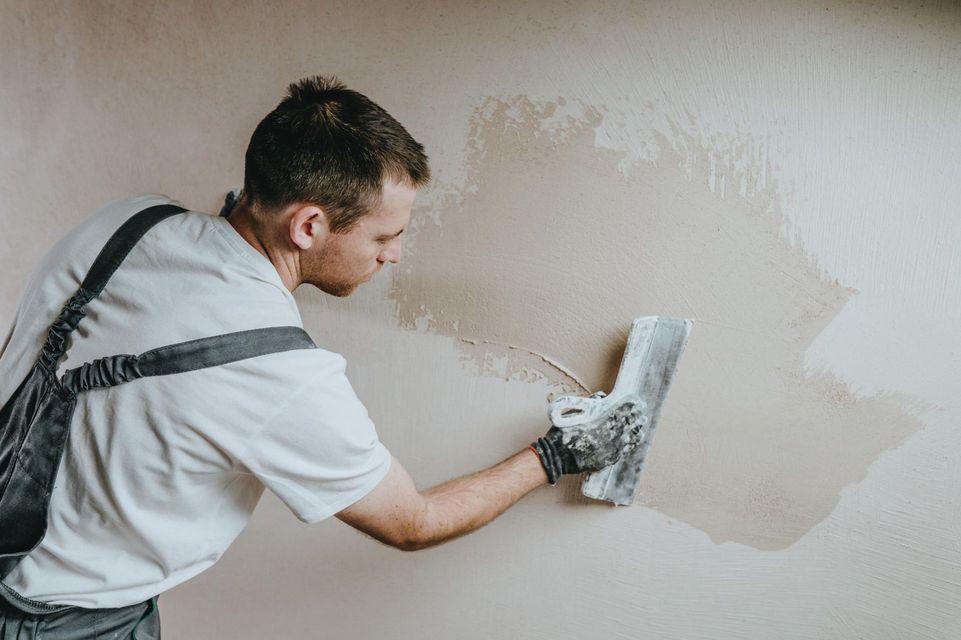 Person plastering a beige wall with a trowel, smoothing fresh paint or plaster.