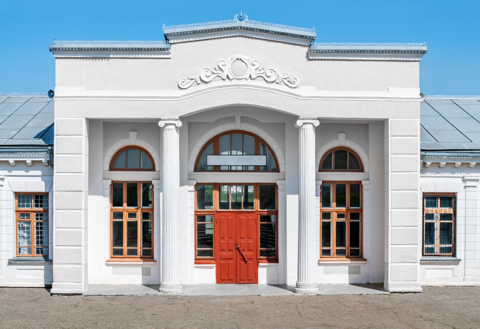White building facade with arched windows and a red double door under a blue roof