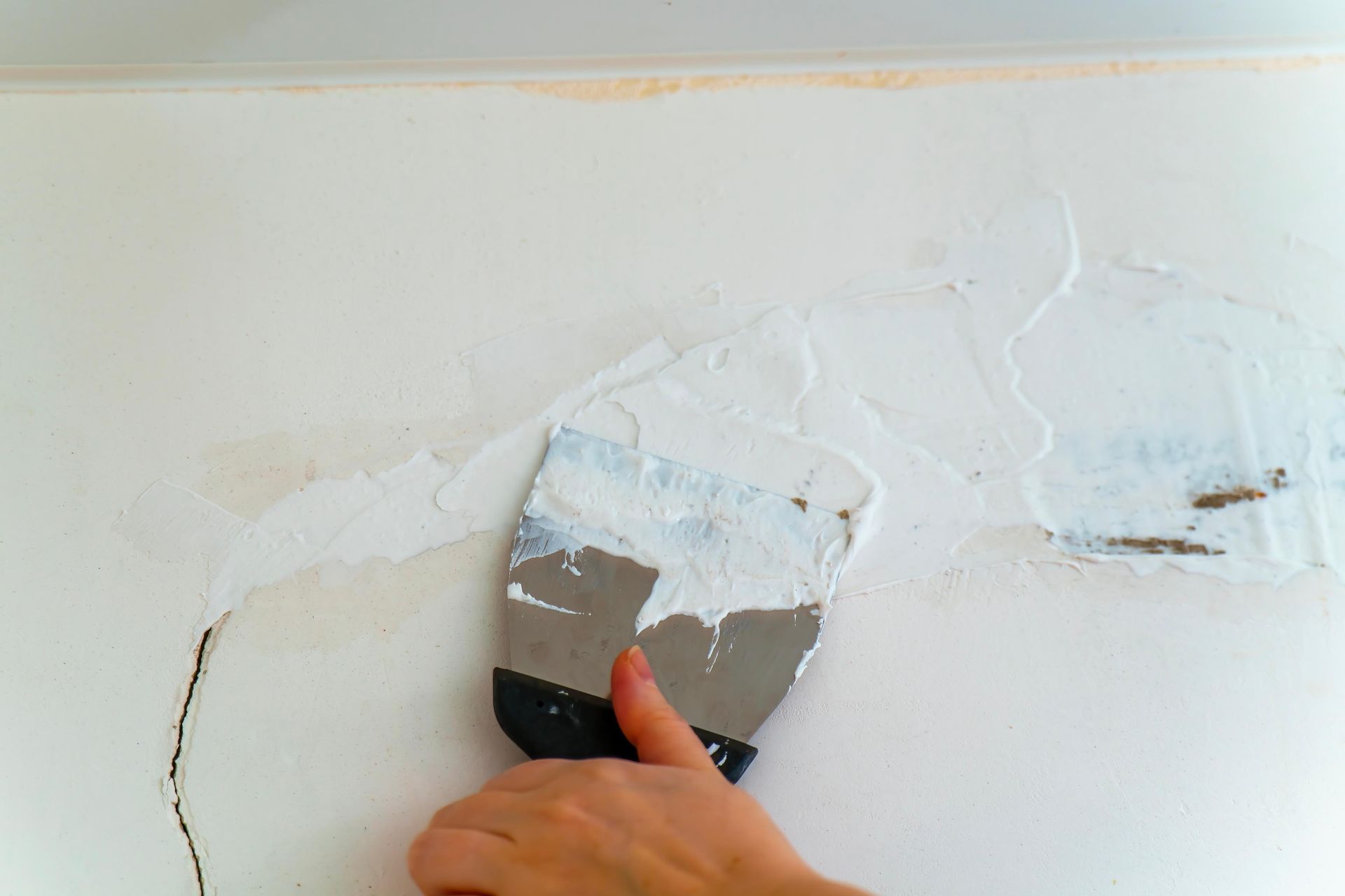 Hand applying white wall filler with a putty knife to a patch on a white wall
