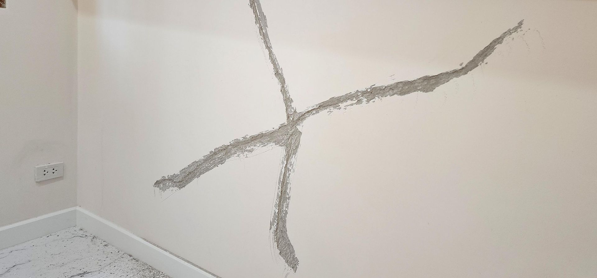 Cracked white wall corner with a long branching fissure near the floor