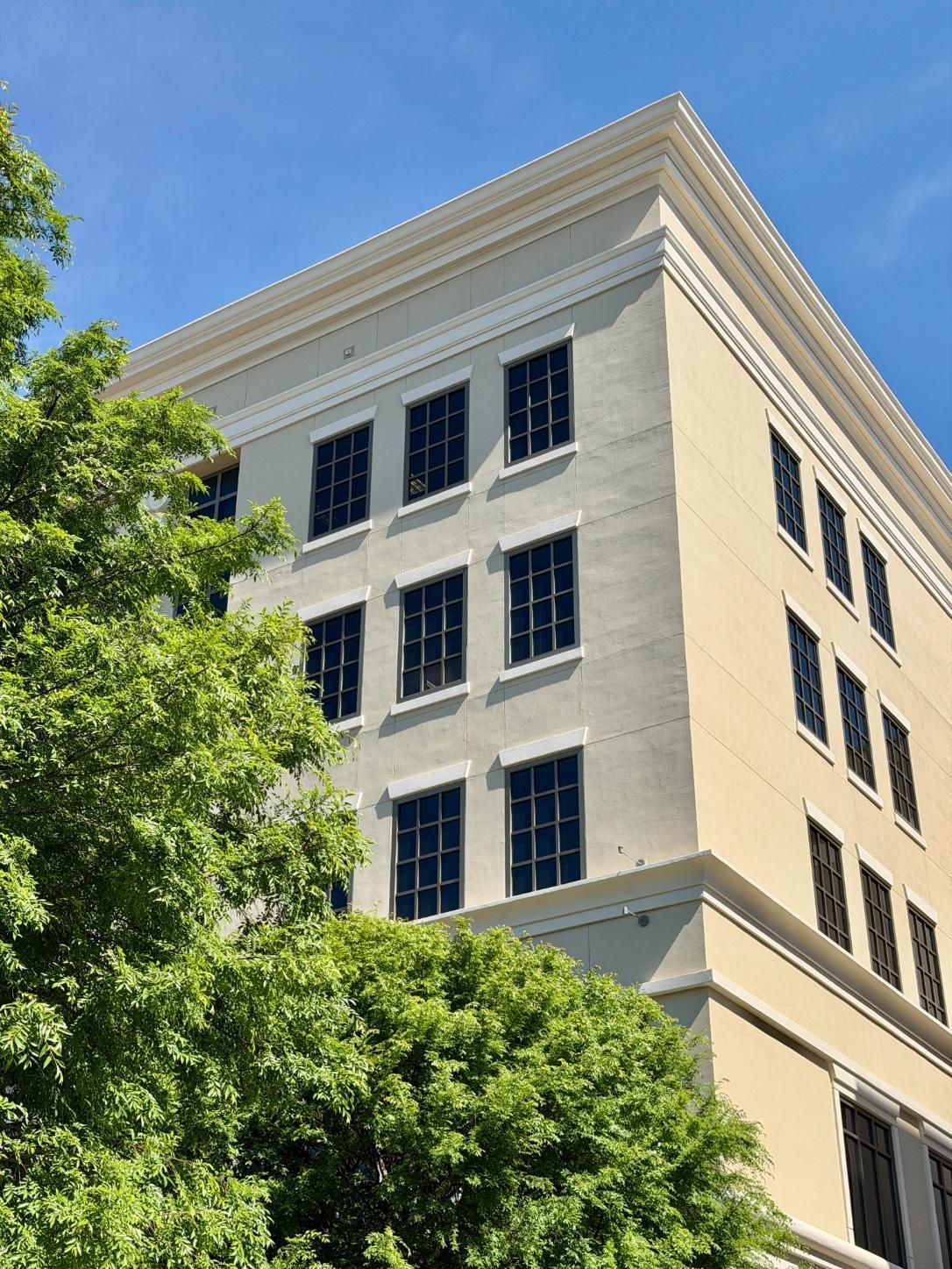 White multi-story building with ornate roofline and blue windows behind green trees