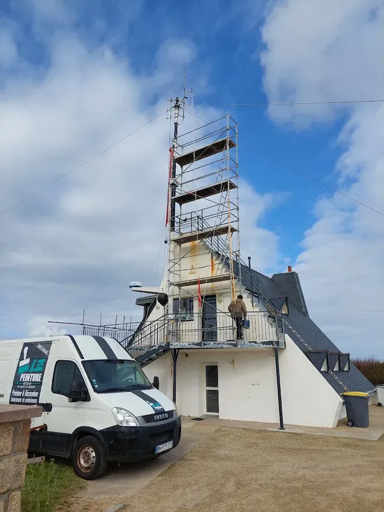 Fourgon utilitaire blanc à côté du clocher élancé d’une église en rénovation, entouré d’échafaudages et d’ouvriers