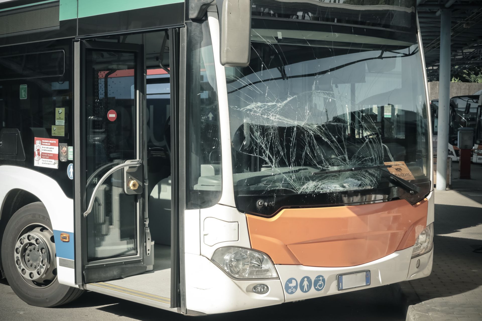 Damaged city bus with shattered windshield and open door at a curb