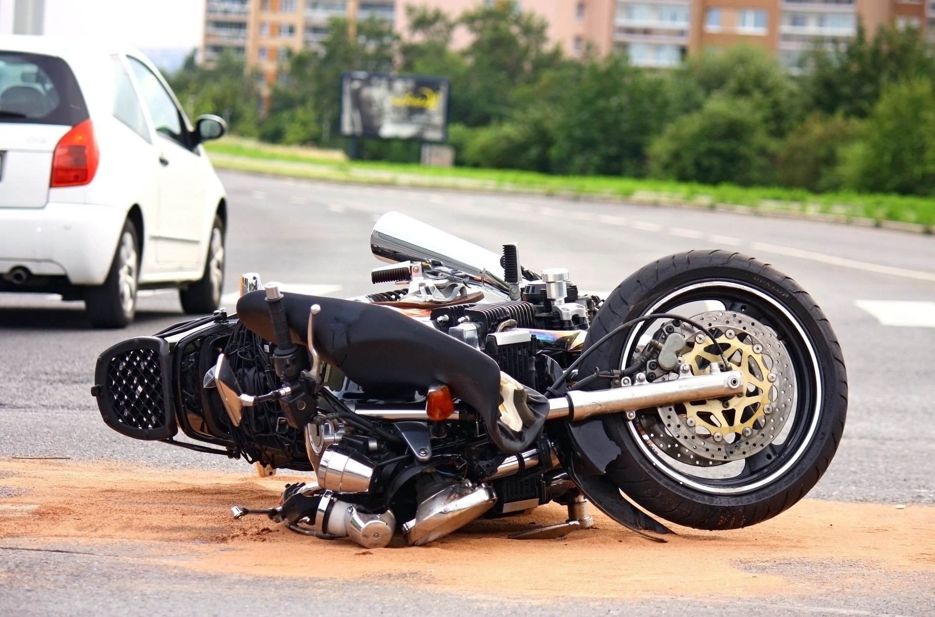 Motorcycle lying on its side after a crash on a wet road beside a white car