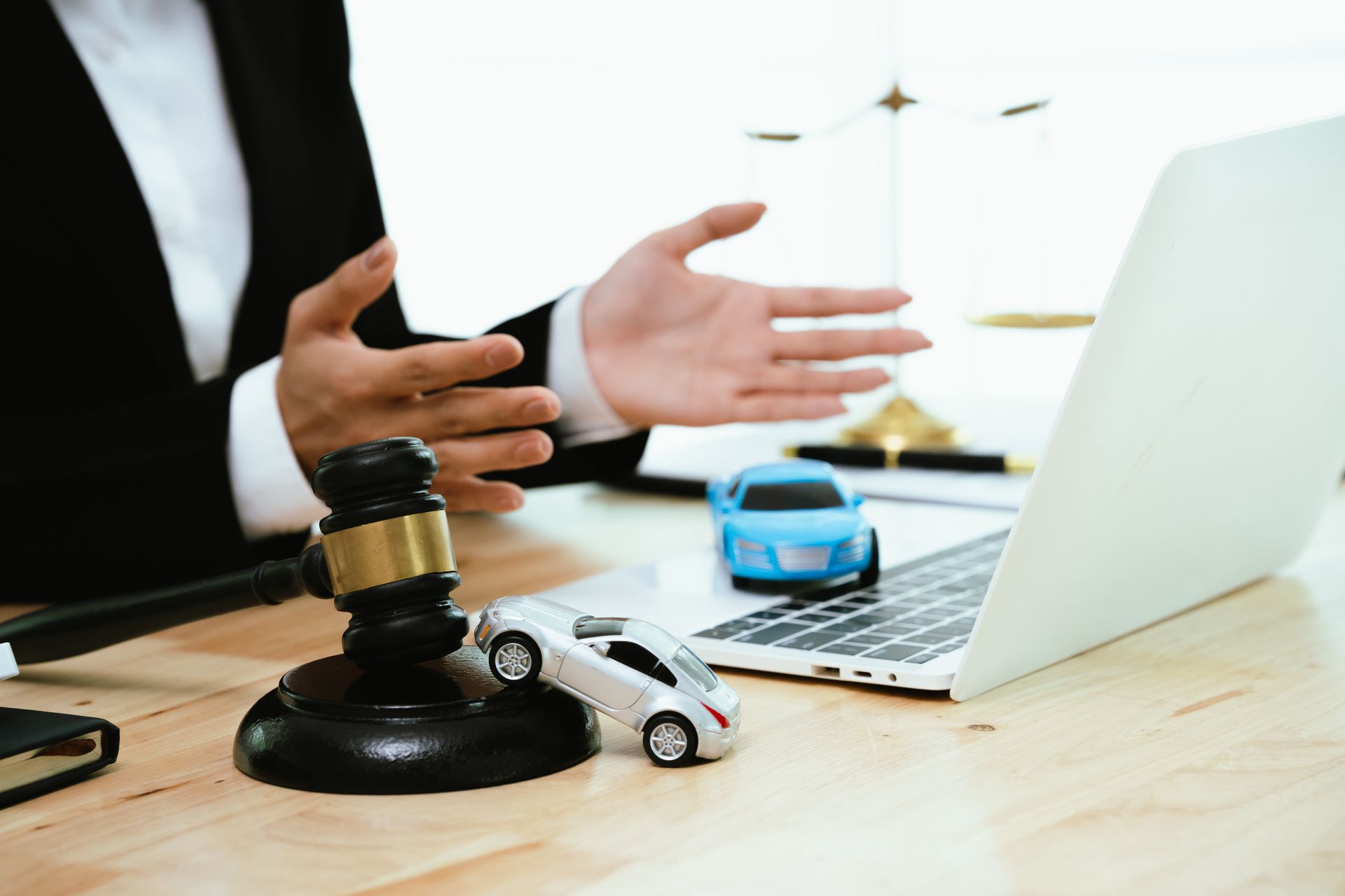 Lawyer gesturing at desk with gavel, toy car, and laptop during accident claim discussion