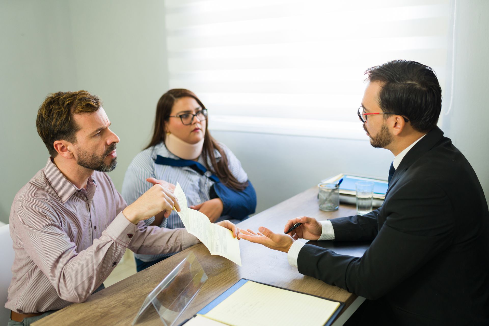Three people in a bright office meeting, discussing papers around a table.