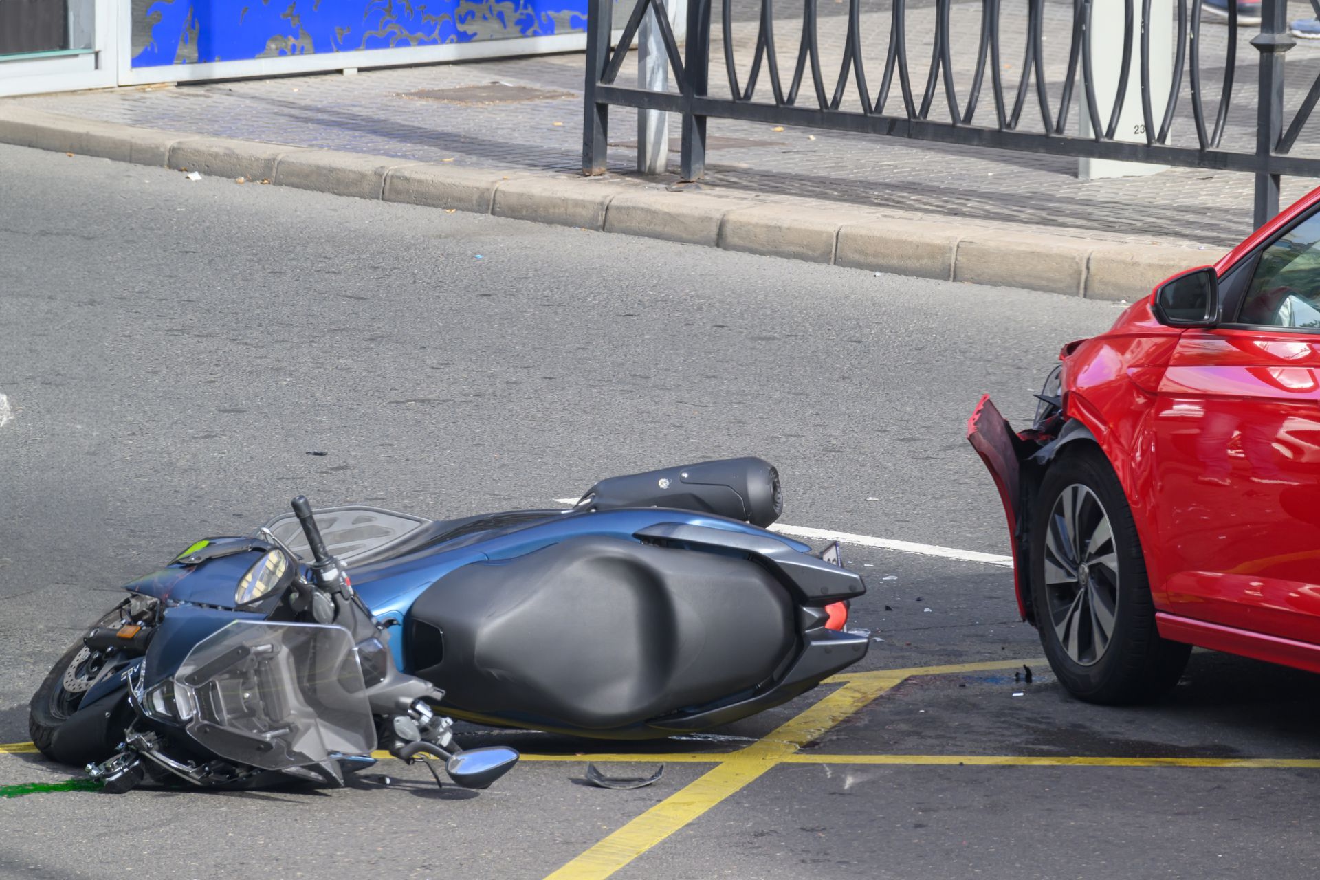 Overturned blue scooter beside a red car on a street curb