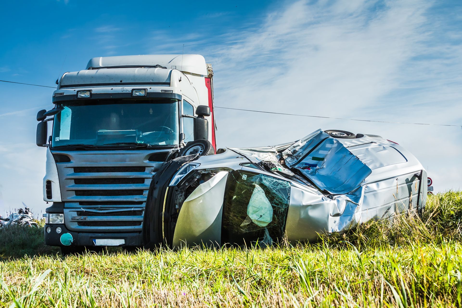 Truck with a crushed car in a grassy field under a blue sky