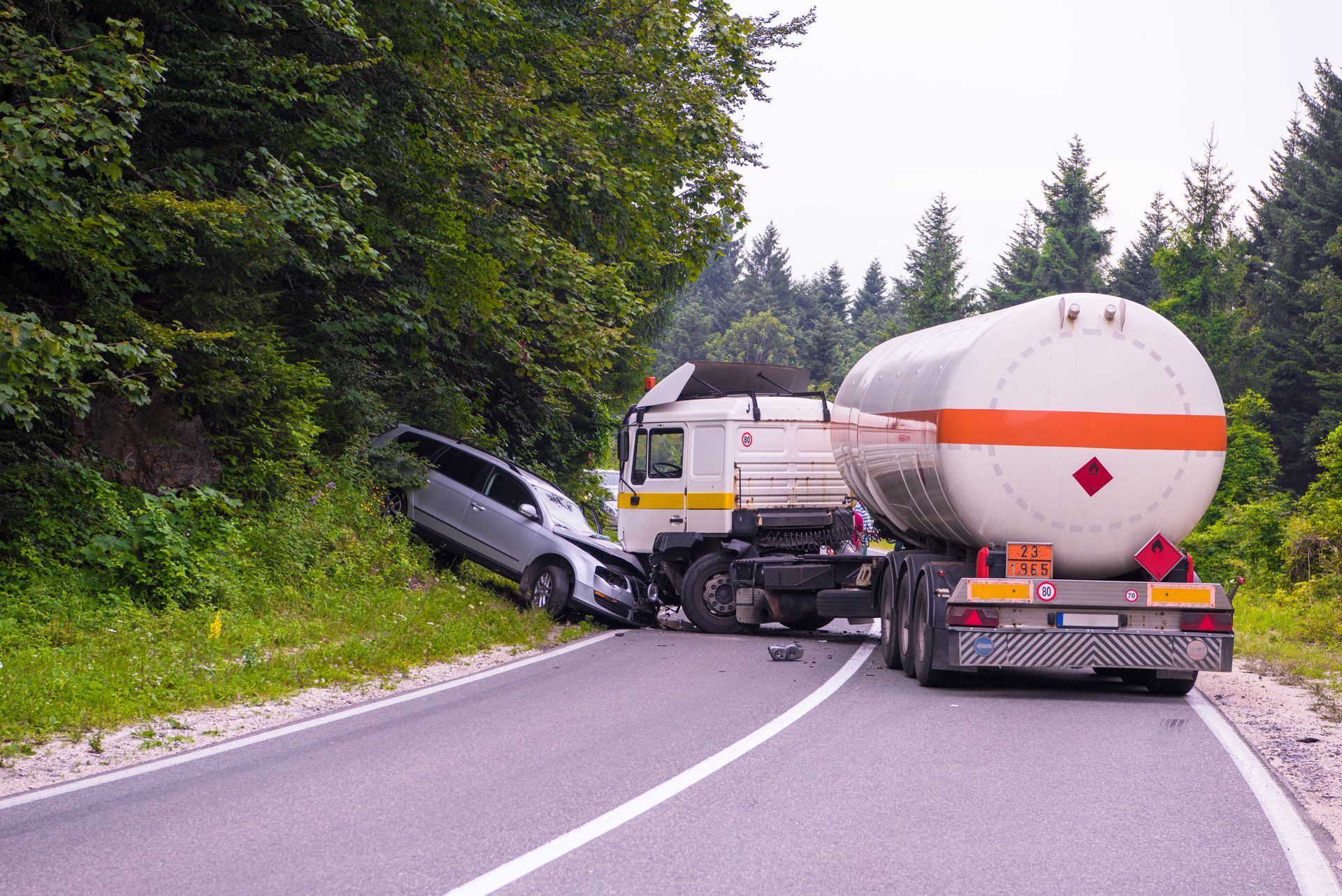 Car crash blocking a winding road, with a tanker truck and wrecked car near a forested roadside