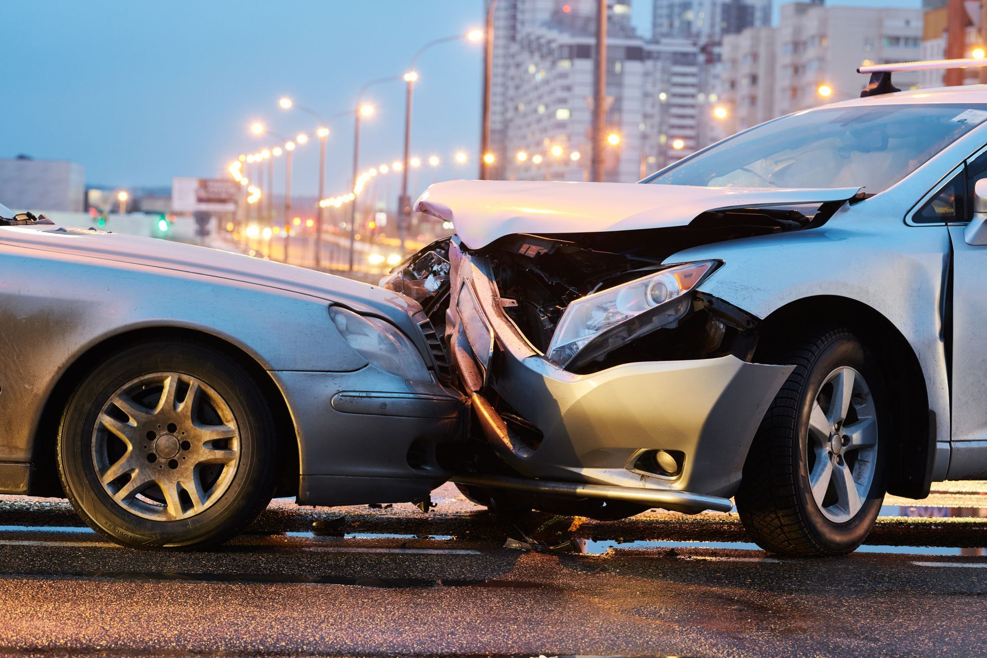 Two cars with severe front-end collision on a wet city street at dusk