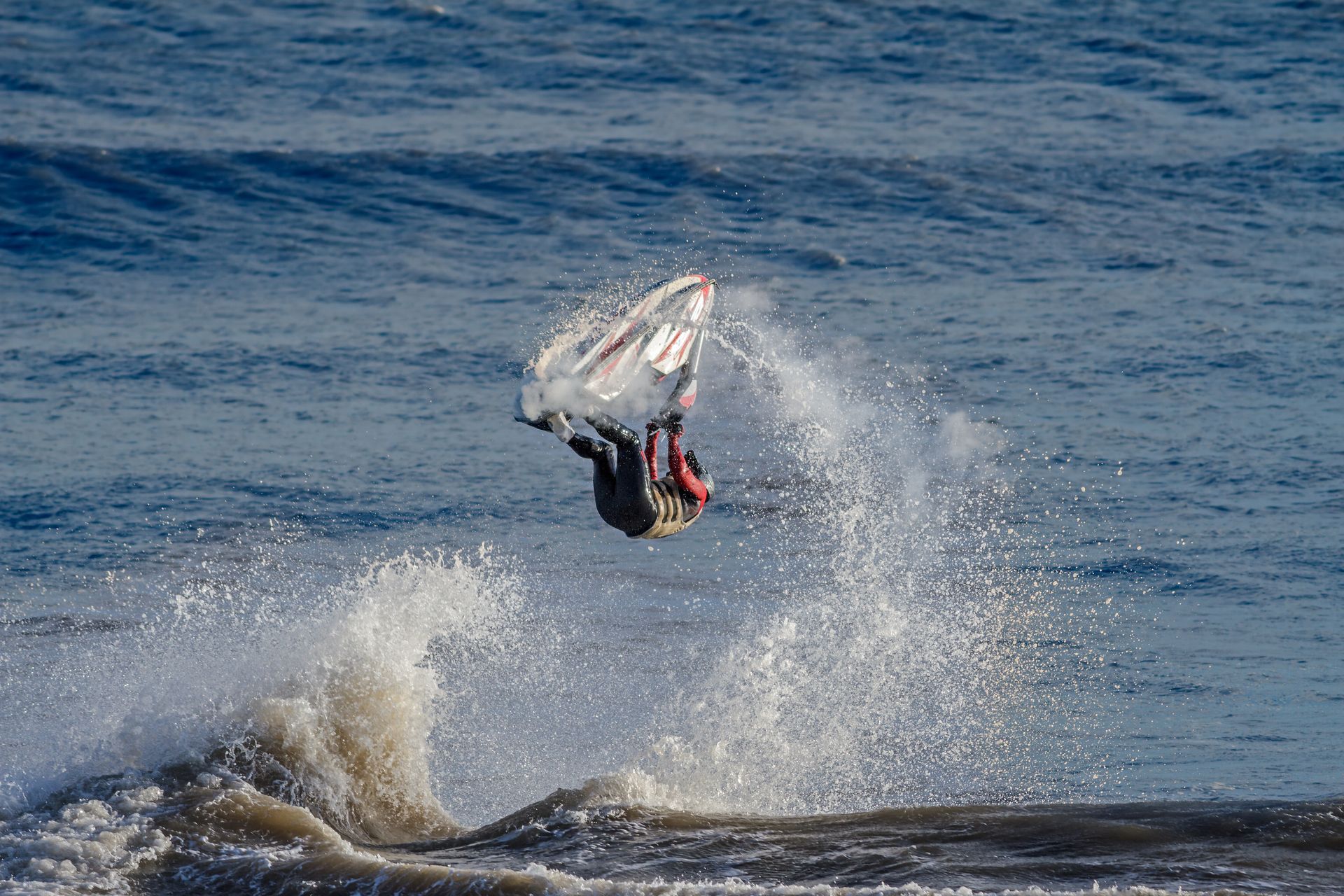 Capsized white sailboat on a shallow beach with waves and blue sky