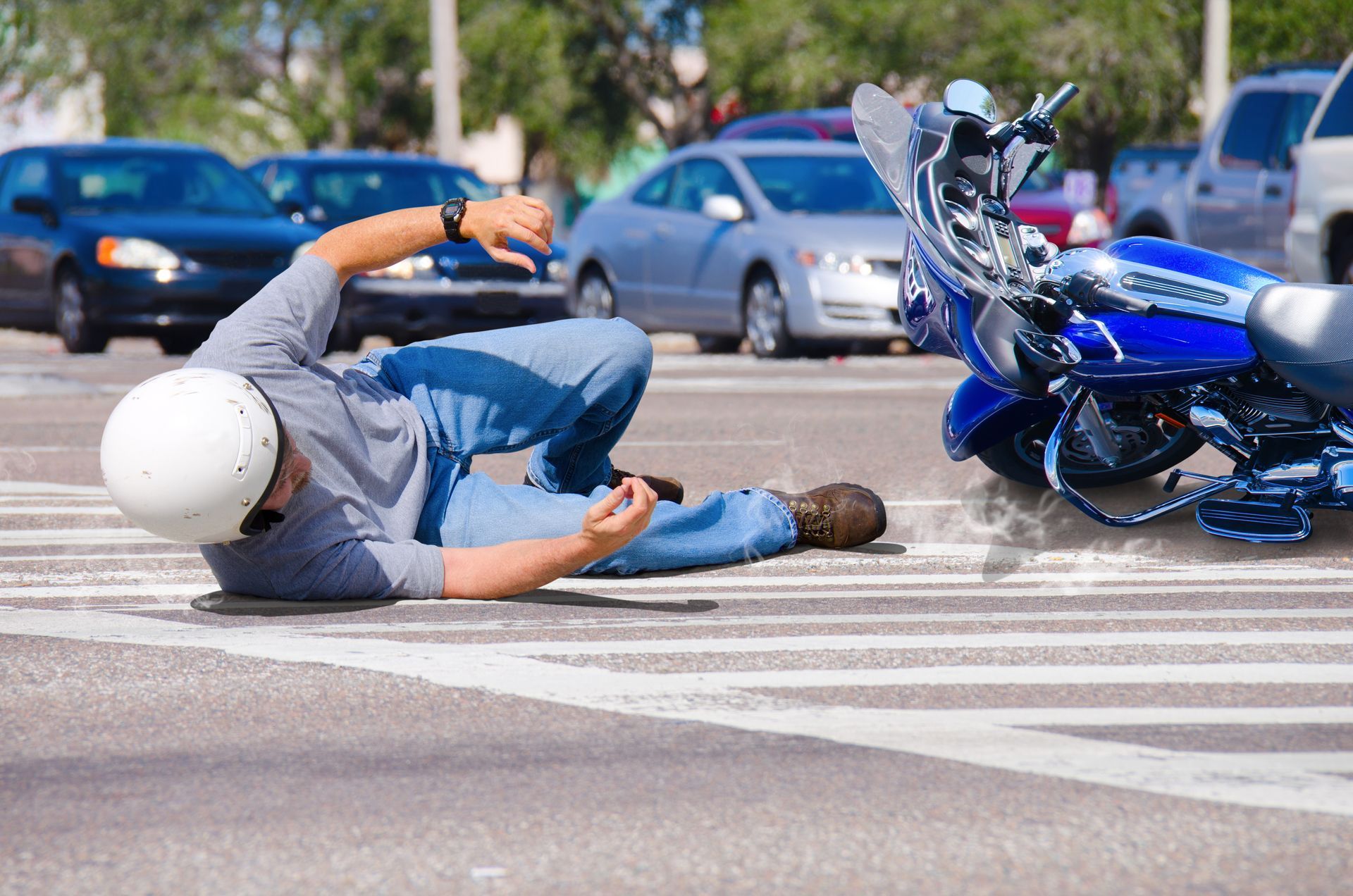 Motorcyclist lying on road beside a crashed blue motorcycle in a parking lot