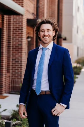 Gunner Sumy, Northwest Missouri-raised personal injury attorney Smiling man in a suit and blue tie standing in a doorway