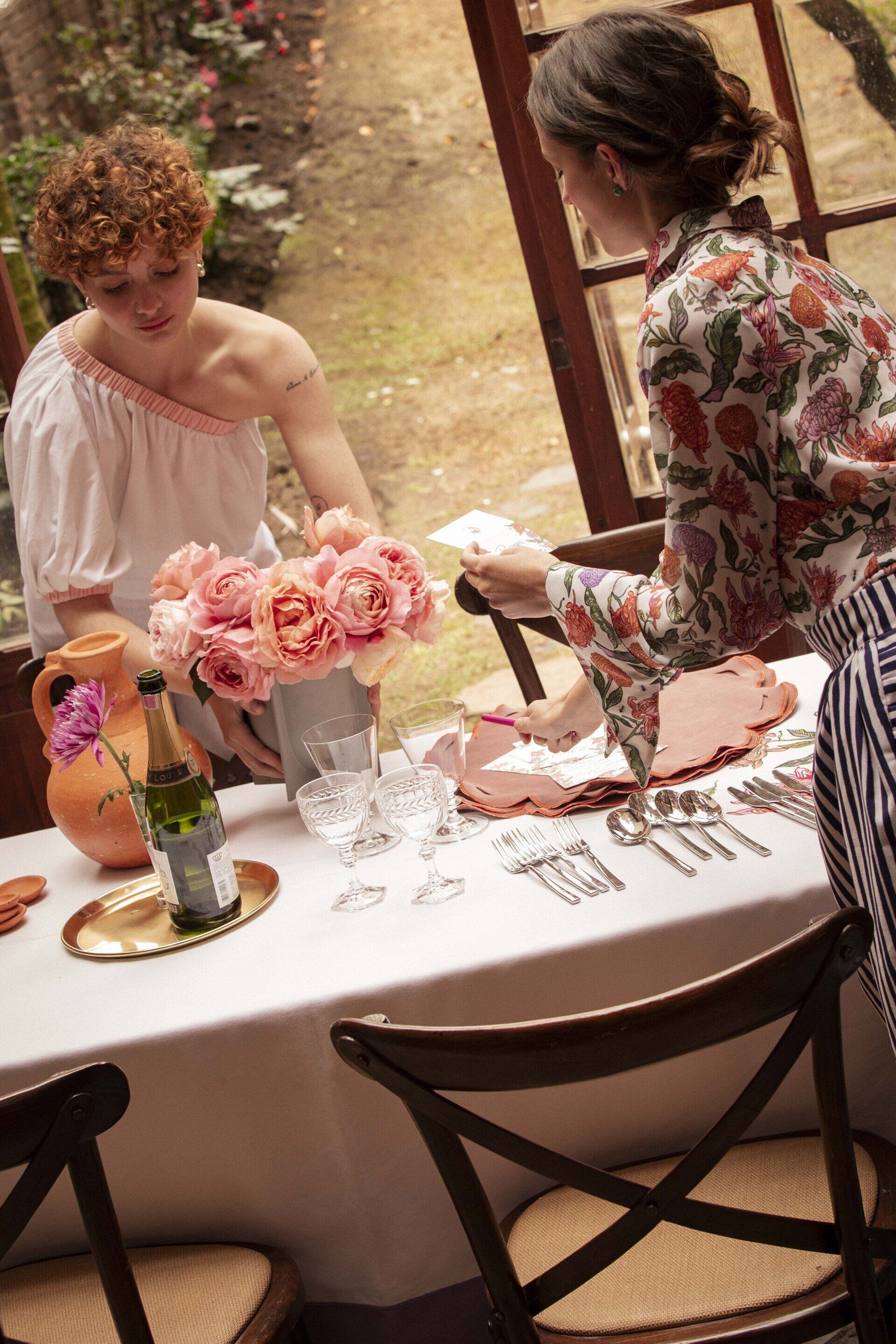 Two women are sitting at a table with flowers on it.