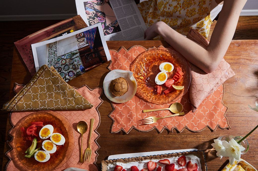 A woman is sitting at a table with plates of food and a magazine.