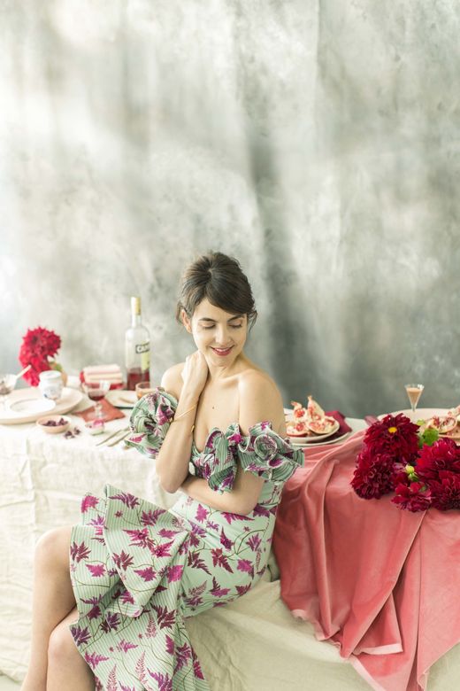 A woman in a floral dress is sitting at a table with flowers.