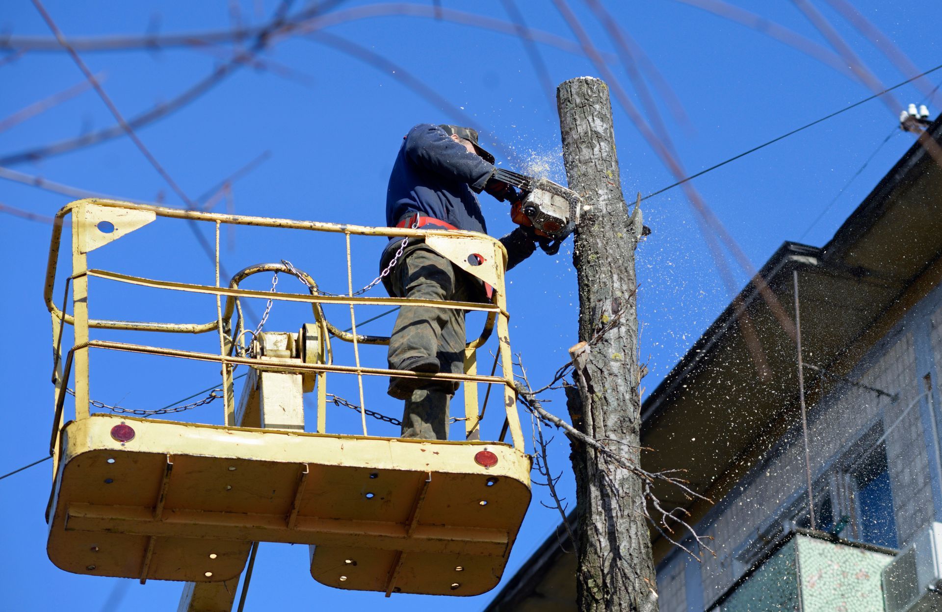 Worker on a yellow lift repairing a utility pole against a blue sky.