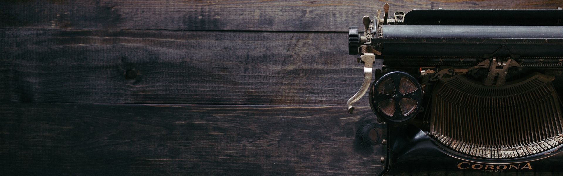 Vintage typewriter on a dark wooden desk with a small lamp, close-up in low light