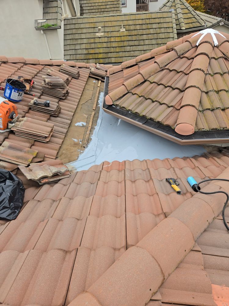 Roofing workers repairing terracotta tile roofs with exposed underlayment and tools on a residential rooftop.