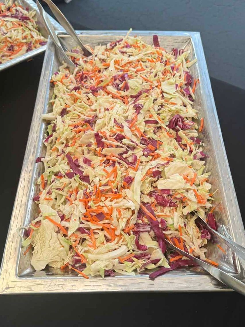 A tray of coleslaw with carrots and cabbage on a table.