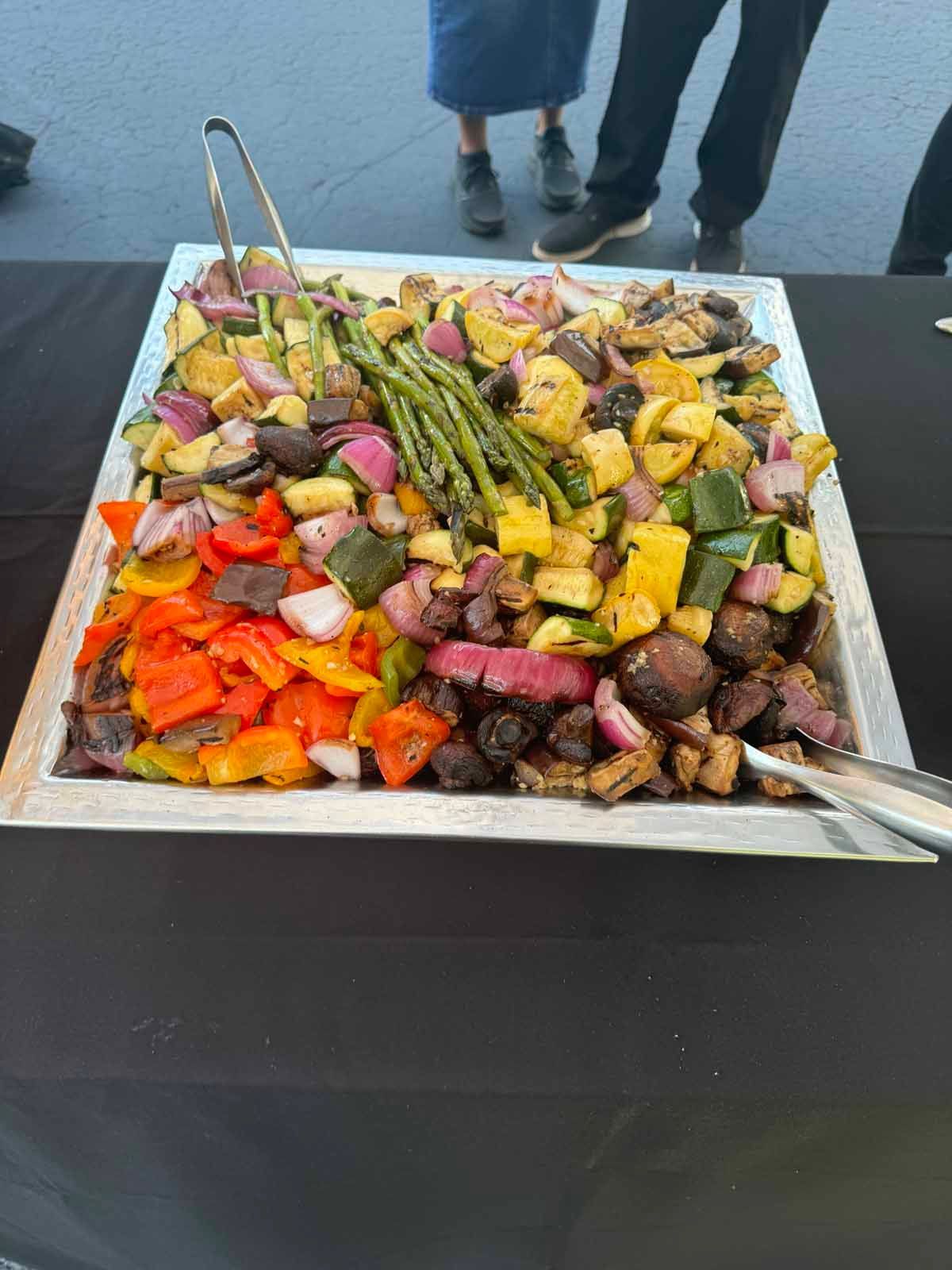 A large tray of vegetables with tongs on a table.