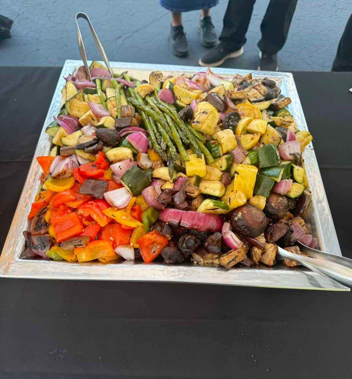 A large tray of vegetables with tongs on a table.