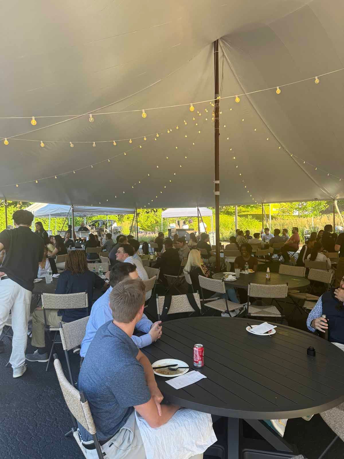 A group of people are sitting at tables under a tent.