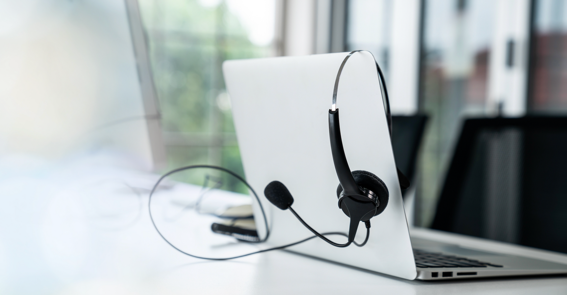 Laptop with attached headset on a white desk, suggesting remote work or communication.