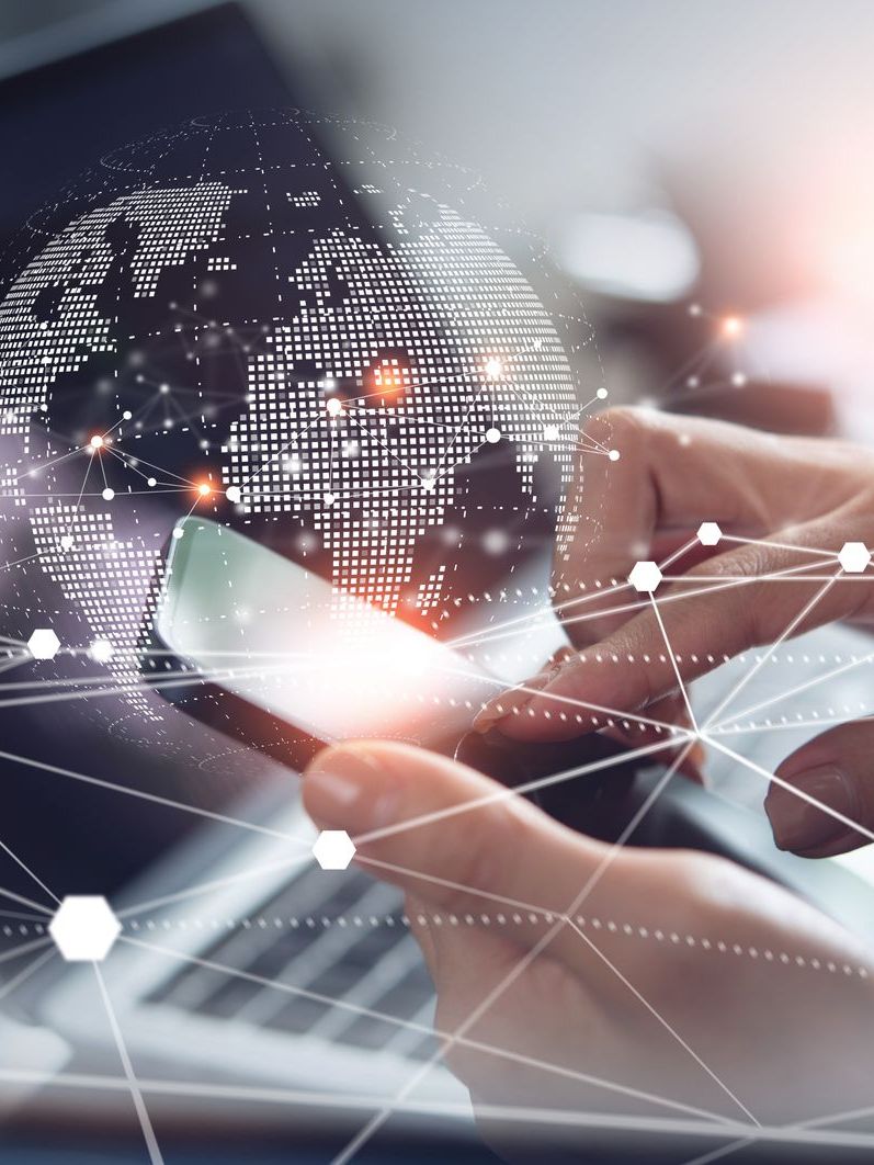 Hands holding a smartphone with a digital globe overlay, connected by lines to a laptop.