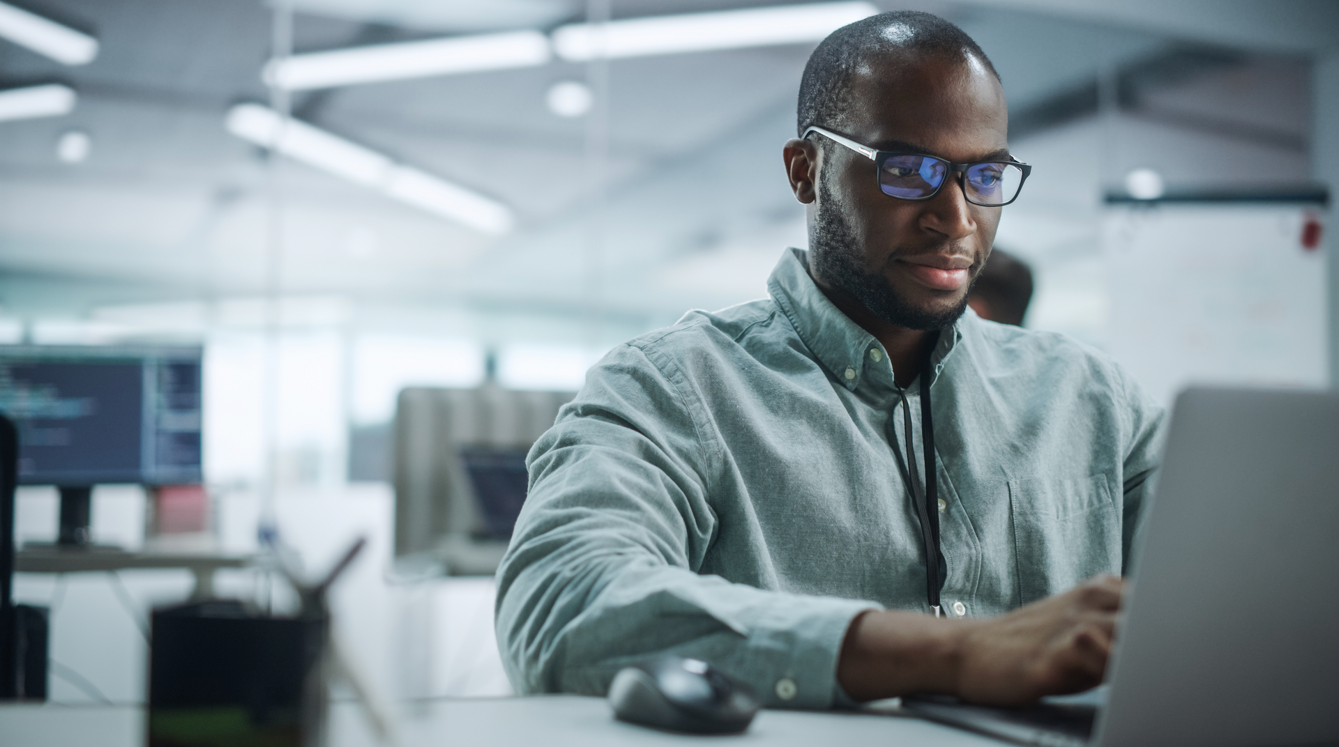 Man in glasses working on a laptop in a modern office, typing with a serious expression.