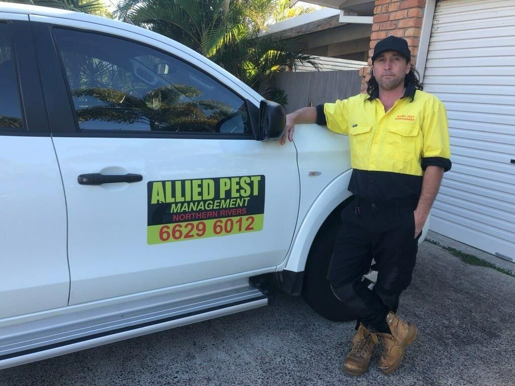 A Man in A Yellow Shirt Is Standing Next to A White Truck — Allied Pest Management Northern Rivers in Pottsville, NSW