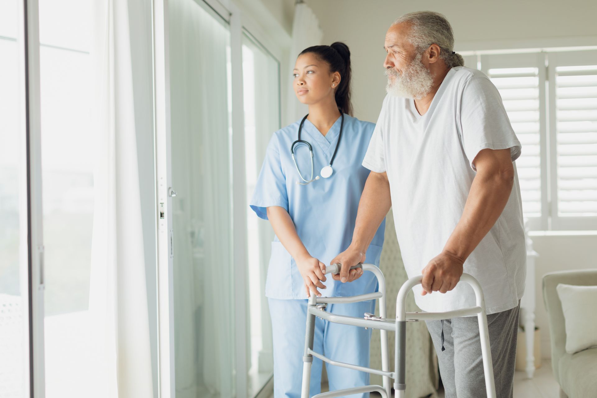 Nurse helping a patient walk with a walker in a bright hospital room