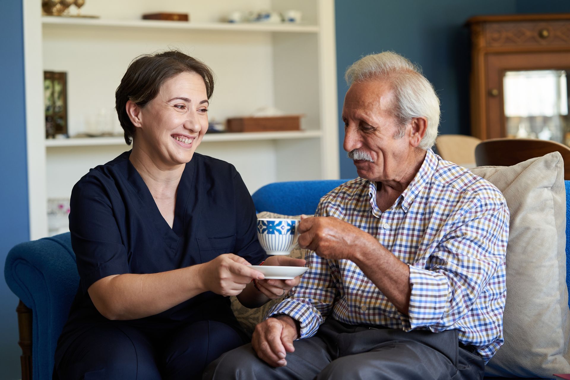 Woman handing a cup to an elderly man on a couch in a bright living room