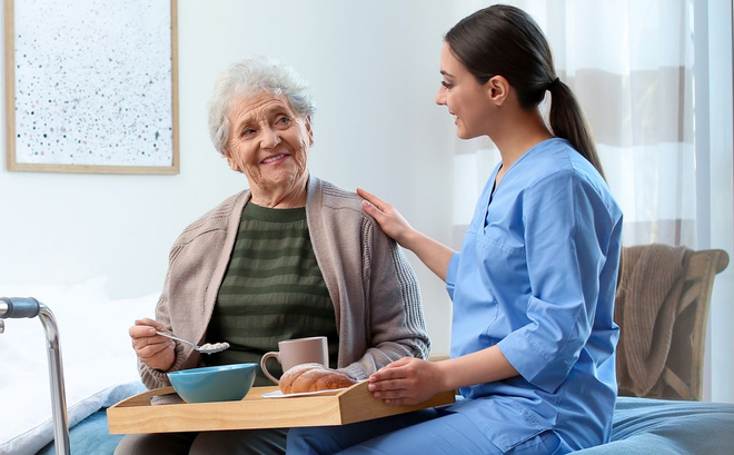 Caregiver in blue uniform comforting an elderly woman seated at a table in a bright living room Caregiver in blue uniform comforting an elderly woman seated at a table in a bright living room
