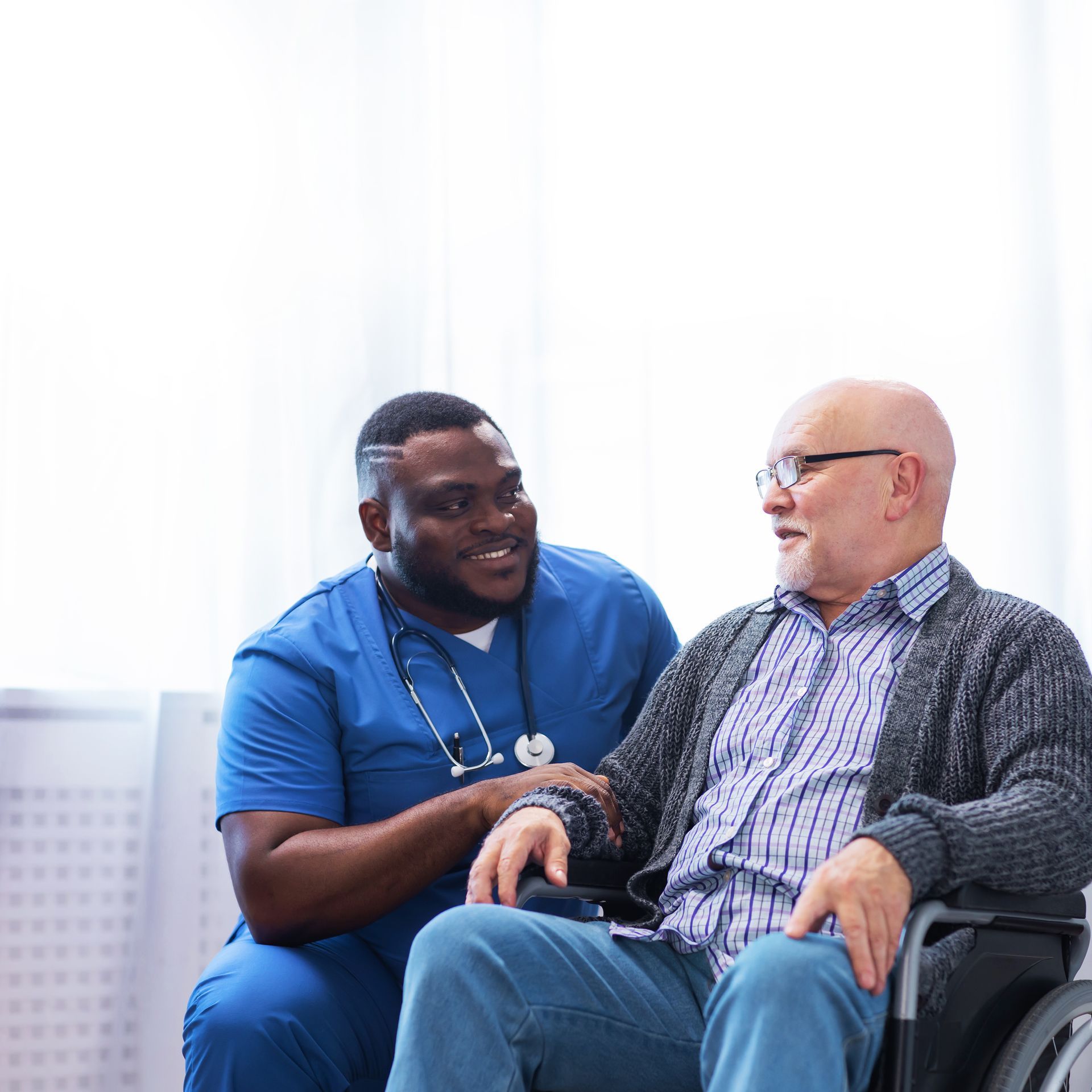 Nurse in blue scrubs talking with a seated patient in a bright clinic room