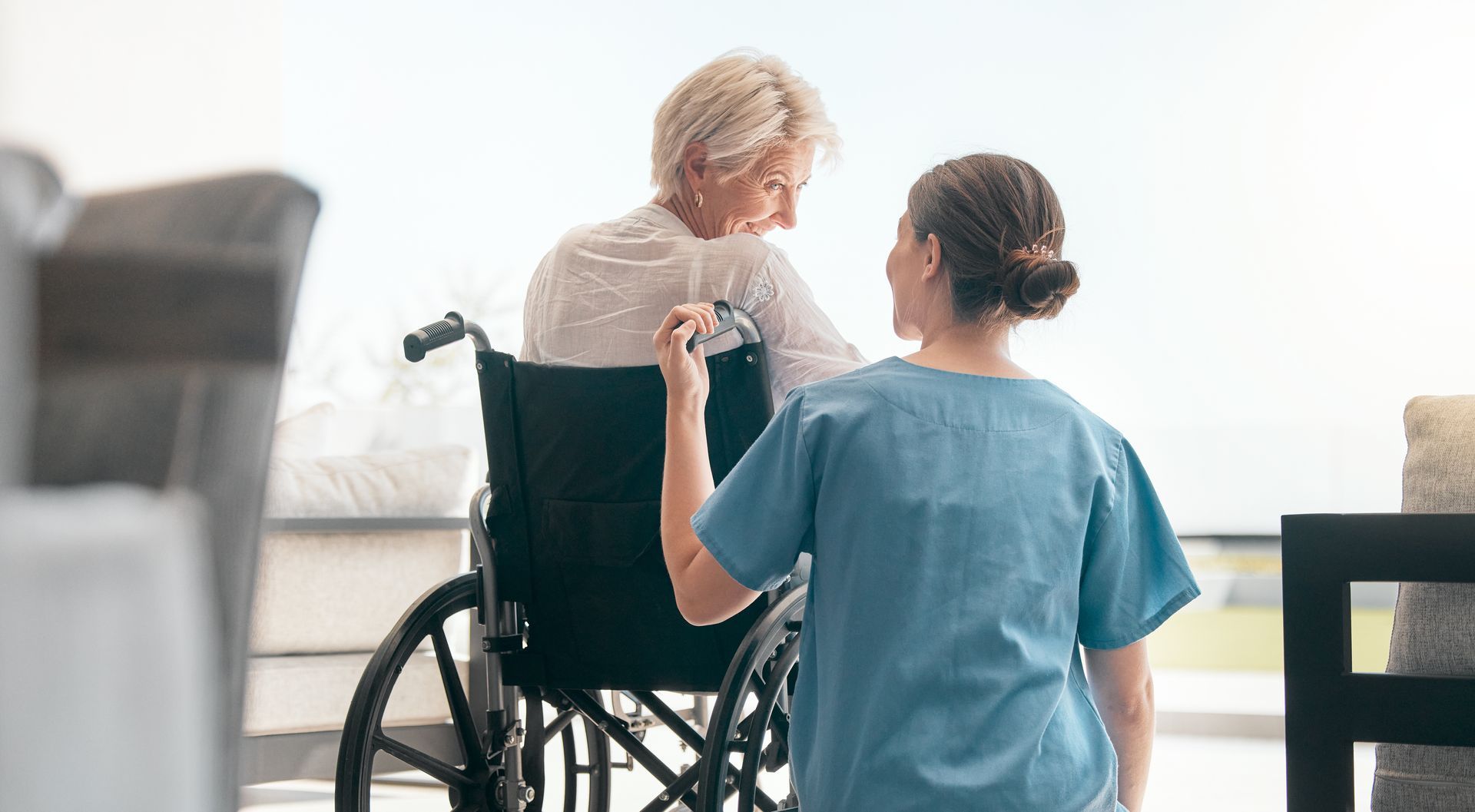Nurse in blue scrubs assisting a wheelchair user in a bright room